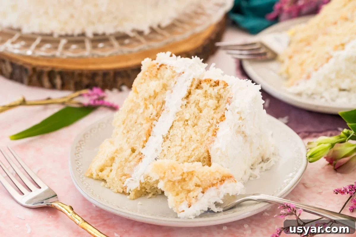 Classic Coconut Cake Recipe with Coconut Cream Frosting 8 Slice of coconut cake on white plate with forkful missing. Pink background with flowers.
