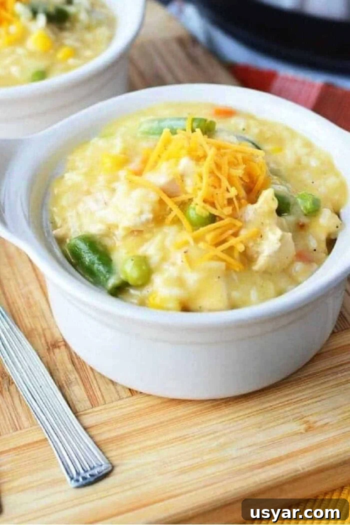 Slow Cooker Cheesy Chicken Casserole Recipe 2 A bowl of creamy chicken and rice topped with shredded cheese on a wooden board, reminiscent of a comforting crockpot chicken casserole, sits invitingly beside a fork.
