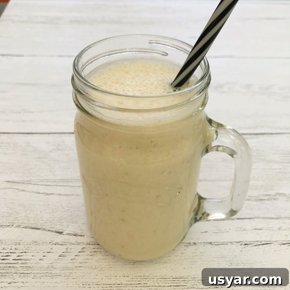 Homemade Peach and Strawberry Juice Recipe 3 white wooden table with kilner jar filled with homemade banana milkshake with black and white straw.