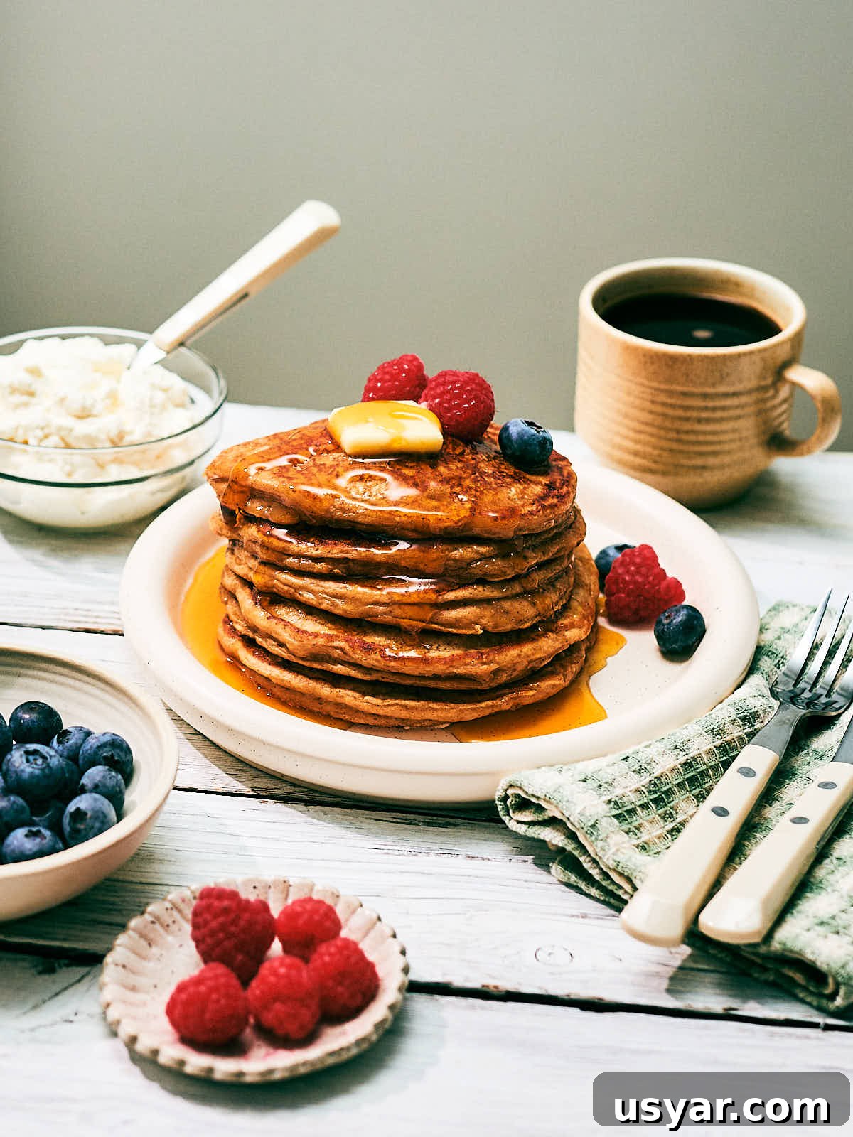 High-Protein Cottage Cheese Pancakes Recipe 11 A stack of high protein Cottage Cheese pancakes on a plate with berries, maple syrup and butter.
