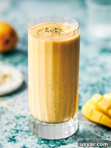 Mango protein smoothie in a glass with hemp seeds sprinkled on top.