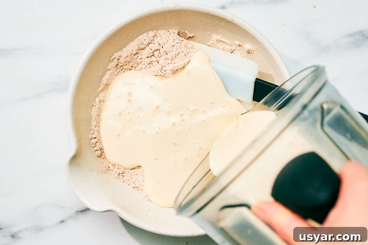 High-Protein Cottage Cheese Pancakes Recipe 8 Adding wet ingredients from blender to dry ingredients in a bowl.