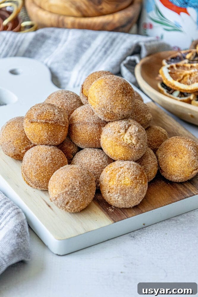 Homemade Baked Cinnamon Sugar Donut Holes Recipe 4 Cinnamon sugar doughnut holes on a cutting board.