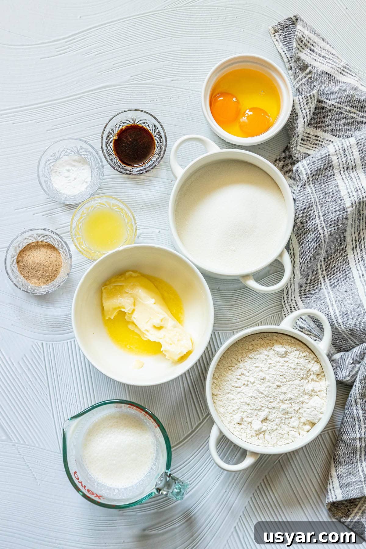 Homemade Baked Cinnamon Sugar Donut Holes Recipe 5 picture of vanilla, flour, sugar, eggs, butter, flour, sugar, salt, and milk in bowls on a table