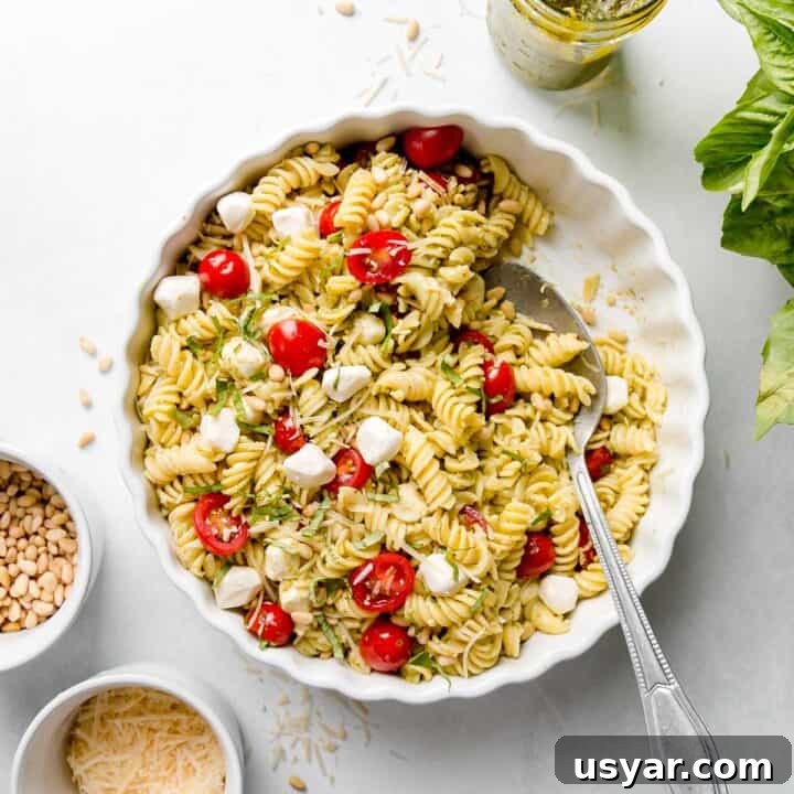 Gluten-free pesto pasta salad in a white dish with tomatoes and mozzarella pearls.