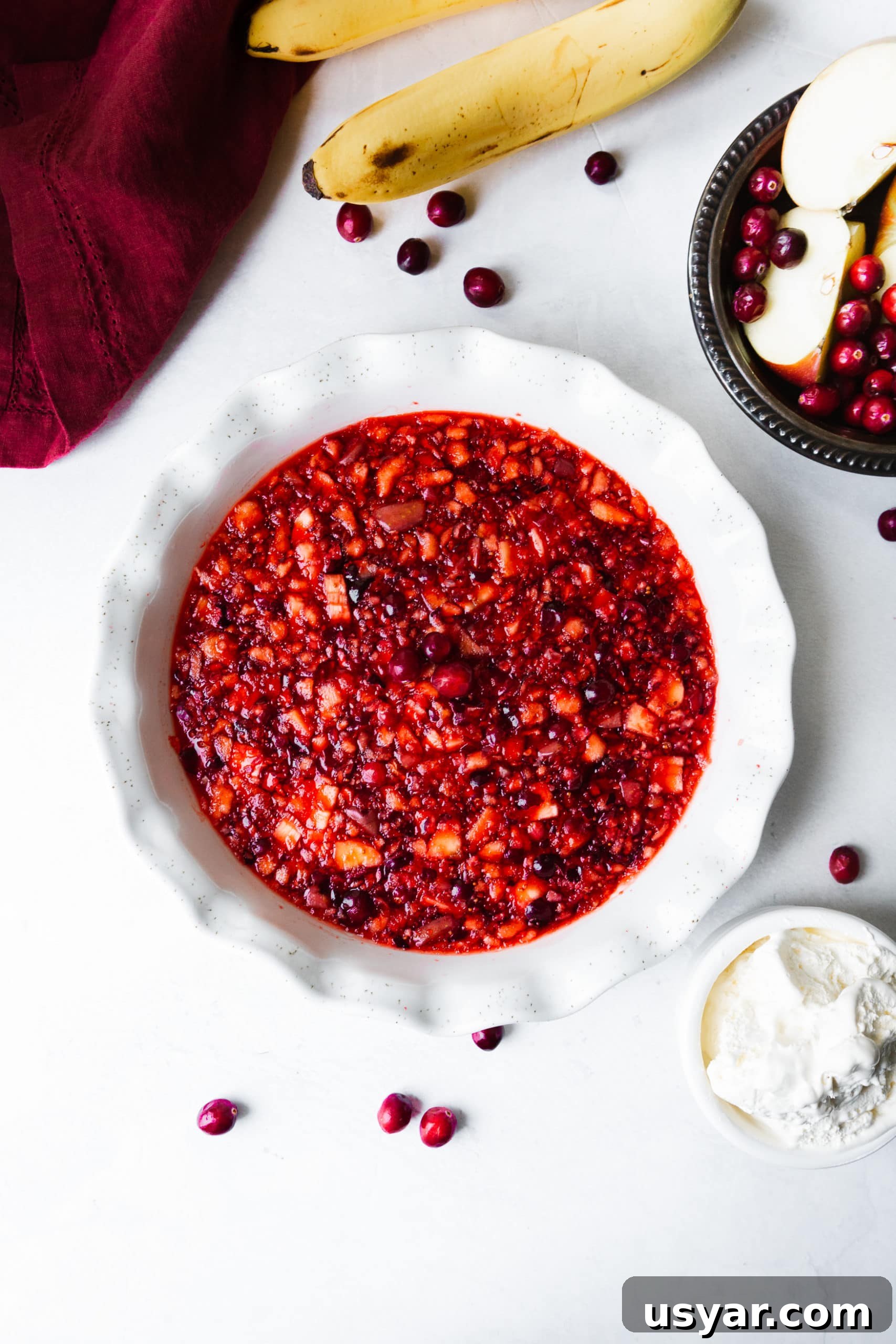 a photo of a white ceramic pie dish full of cranberry jell-o with fresh cranberries scattered around the dish.