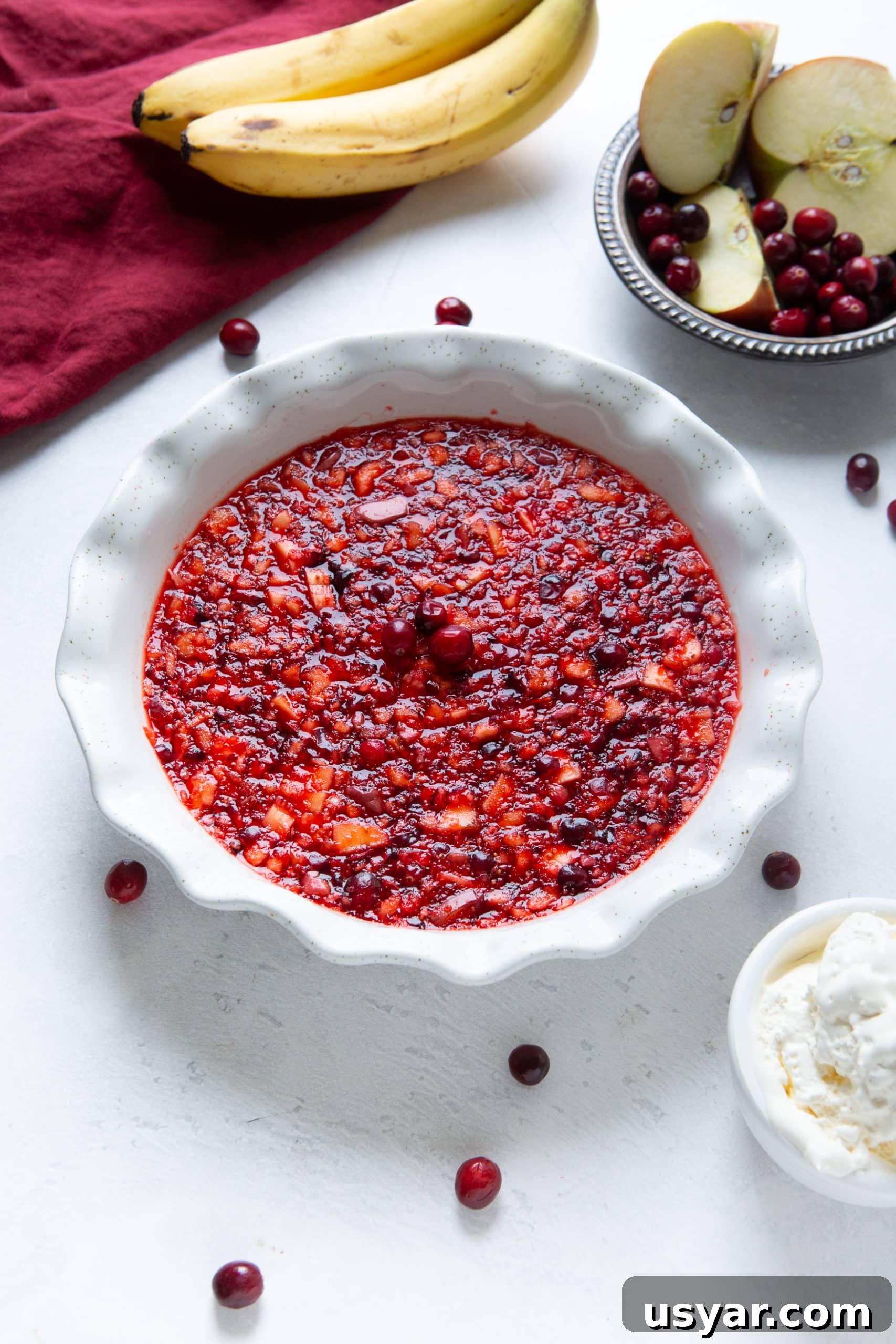 a photo of a white ceramic pie dish that is full of a fruit filled red jello that is topped with three fresh cranberries in the middle.