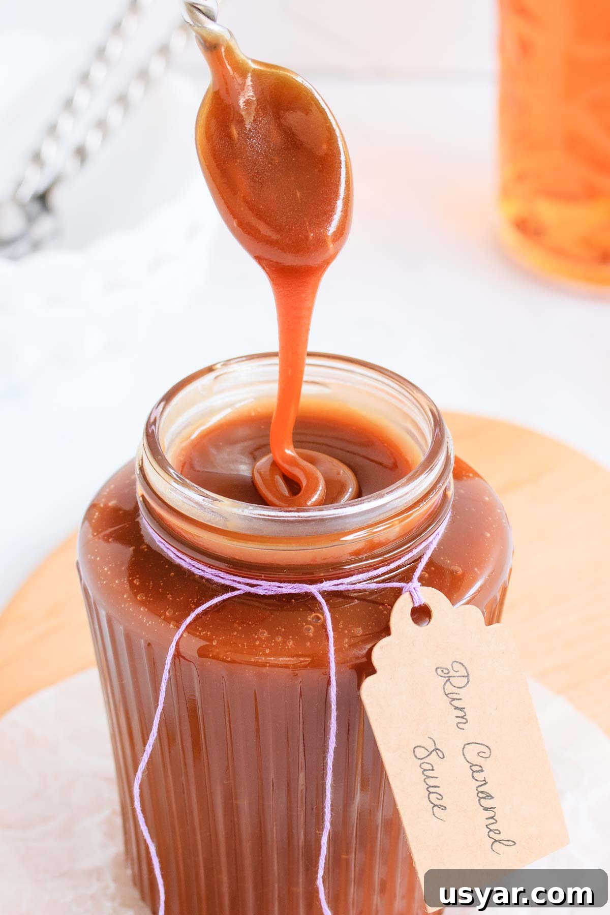 Rum Caramel Sauce Recipe 2 Caramel sauce in a ribbed glass jar with a spoon, text overlay reads rum caramel sauce.