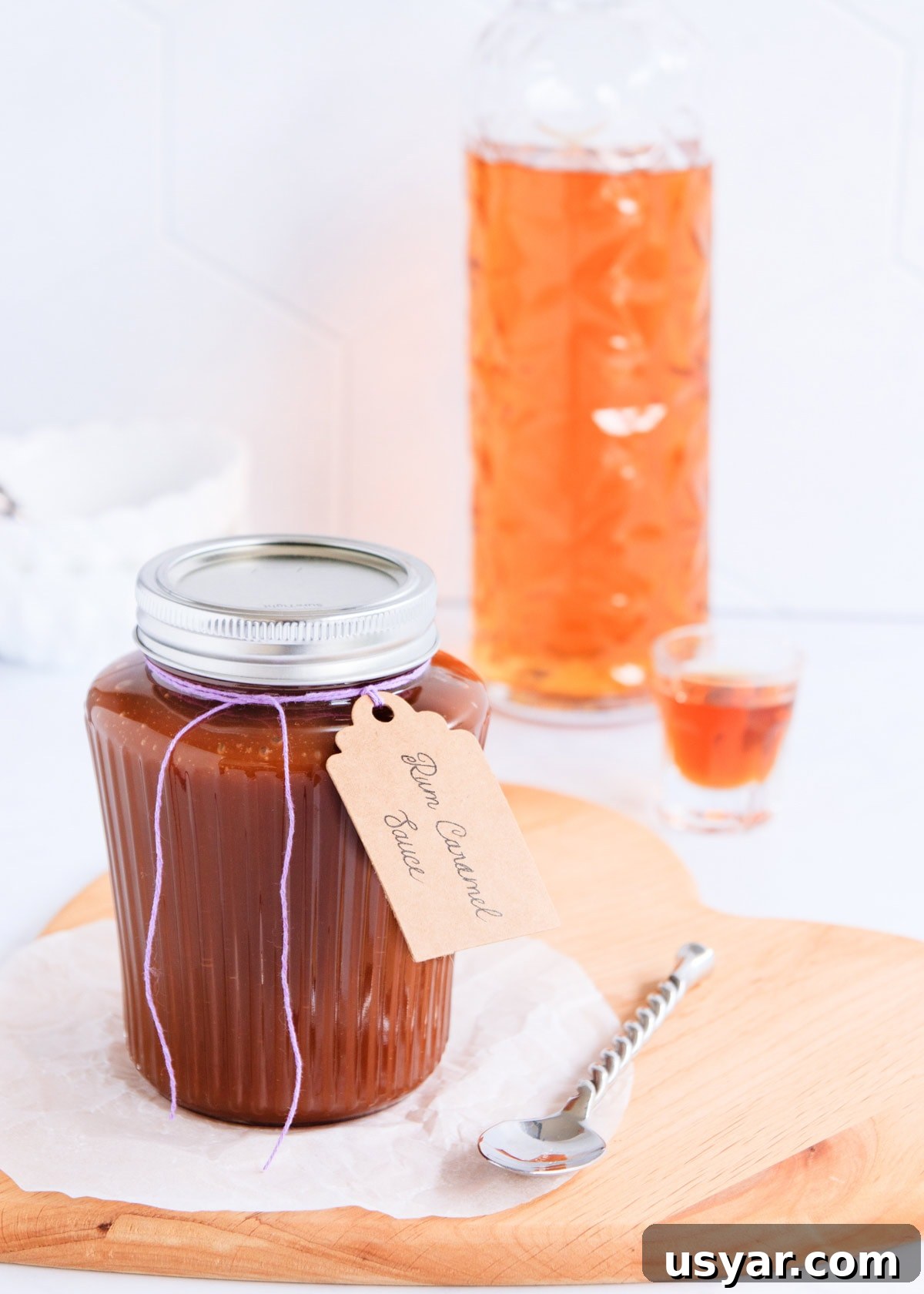 Rum Caramel Sauce Recipe 3 Rum caramel in a ribbed glass jar with a silver lid and a handwritten label tied on with purple twine.