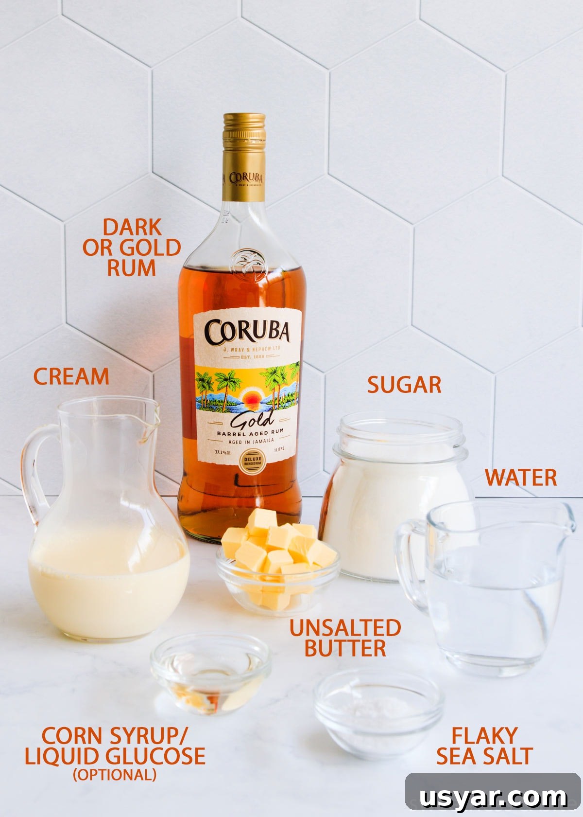Rum Caramel Sauce Recipe 4 Rum caramel sauce ingredients on a grey background with orange text labels: rum, sugar, cream, water, butter, corn syrup and salt.