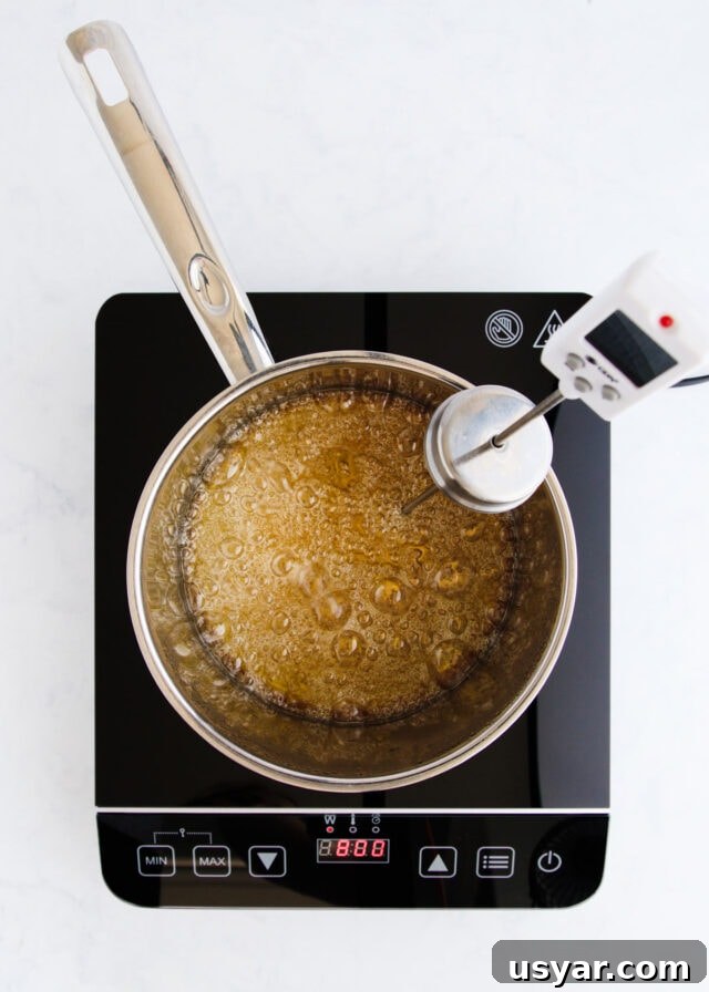 Rum Caramel Sauce Recipe 7 The caramel beginning to turn golden, with a sugar thermometer clipped to the side of the pan.