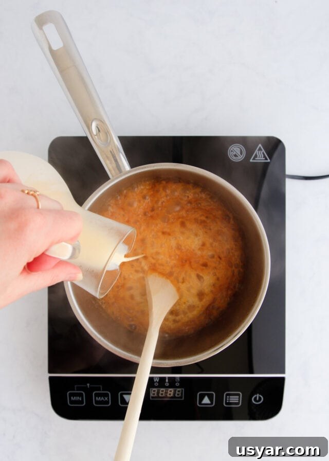 Rum Caramel Sauce Recipe 9 The cream being poured into the caramel from a small glass jug.