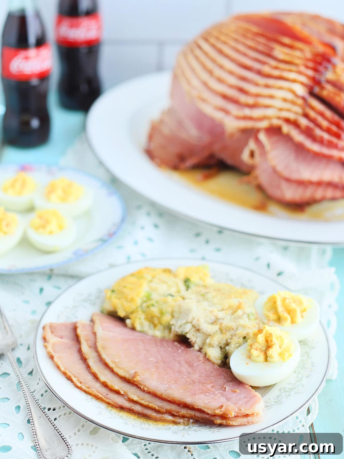 Coca Cola Glazed Ham Recipe 15 Three slices of ham with Coca-Cola glaze on a plate with sides and two deviled eggs.
