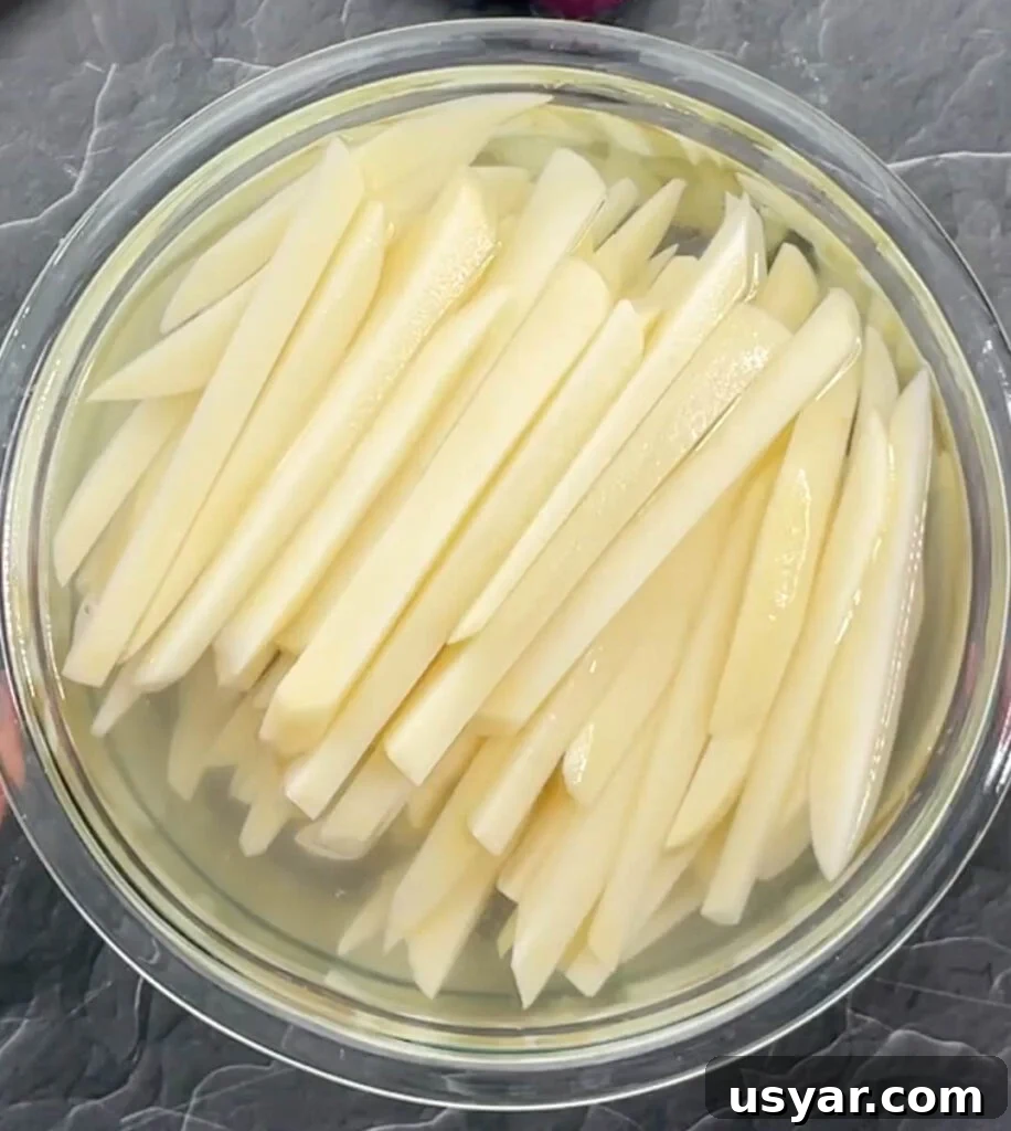 Crispy Homemade Air Fryer French Fries 5 sliced potatoes in a glass bowl of water