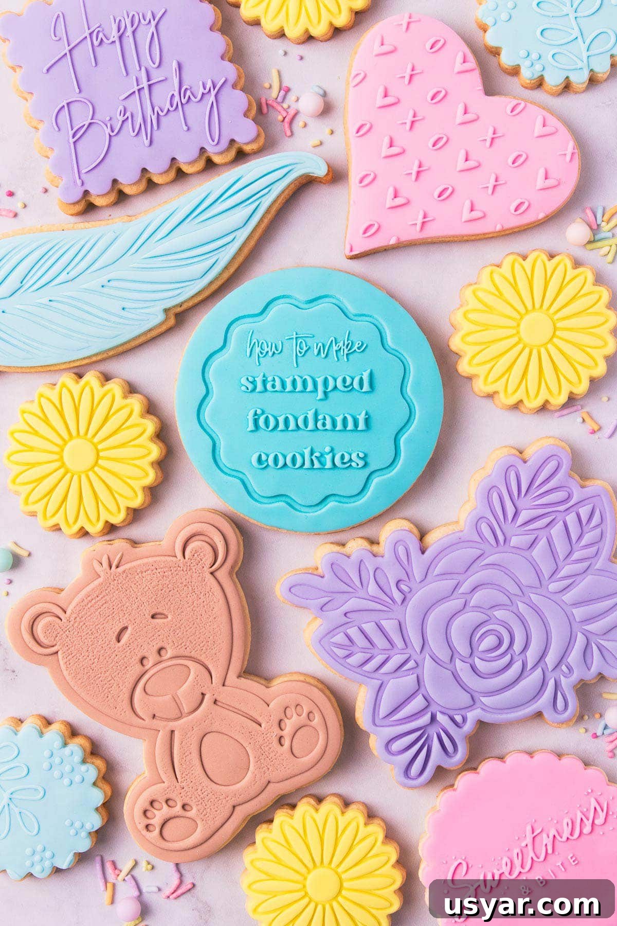 Assorted stamped fondant cookies on a grey background, the middle cookie has a stamped design saying 'how to make stamped fondant cookies'.
