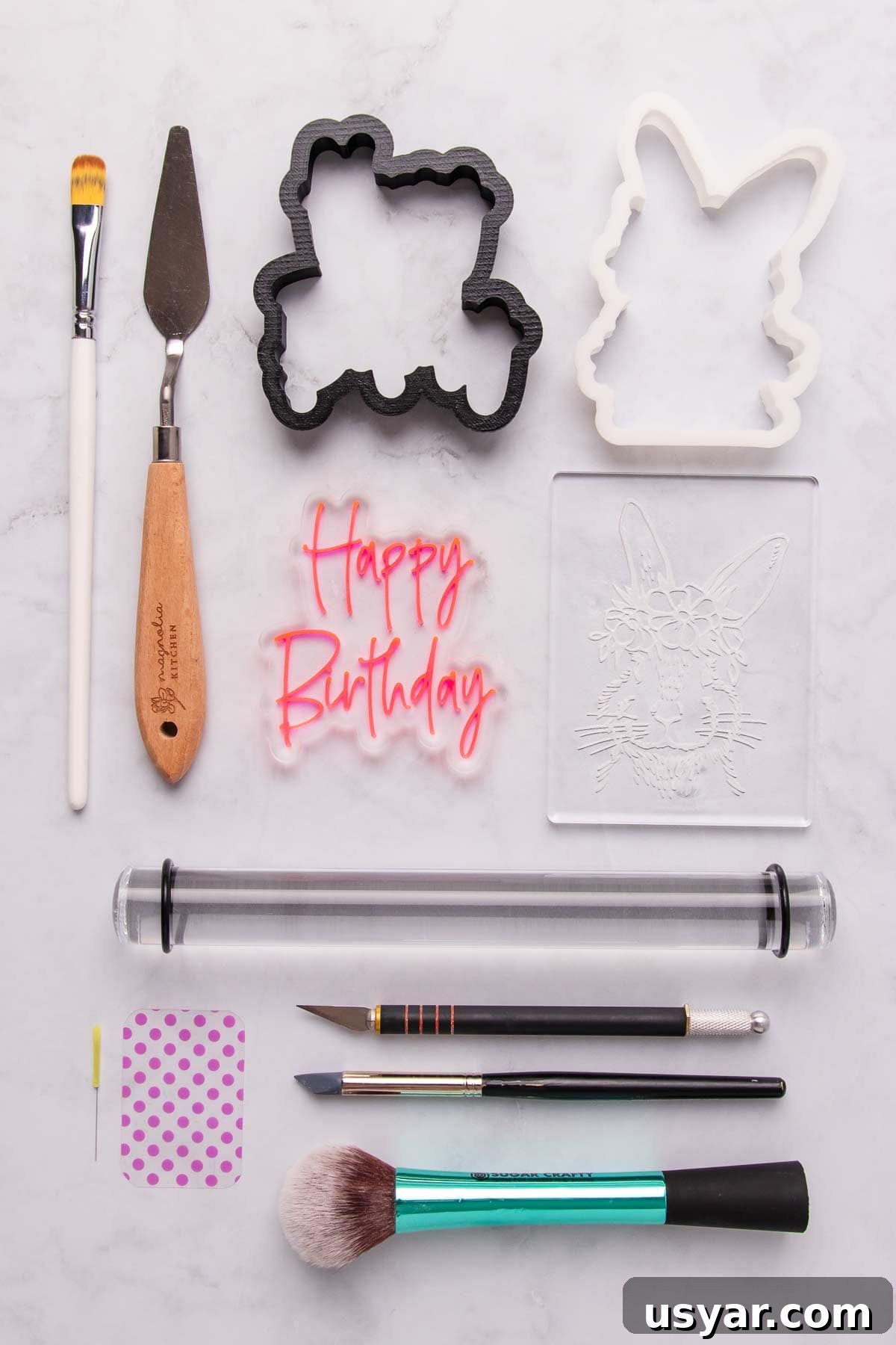 A flat-lay of the tools needed to make stamped fondant cookies - stamps, cookie cutters, rolling pin, fondant smoothers, paintbrushes, a palette knife and a modelling tool.