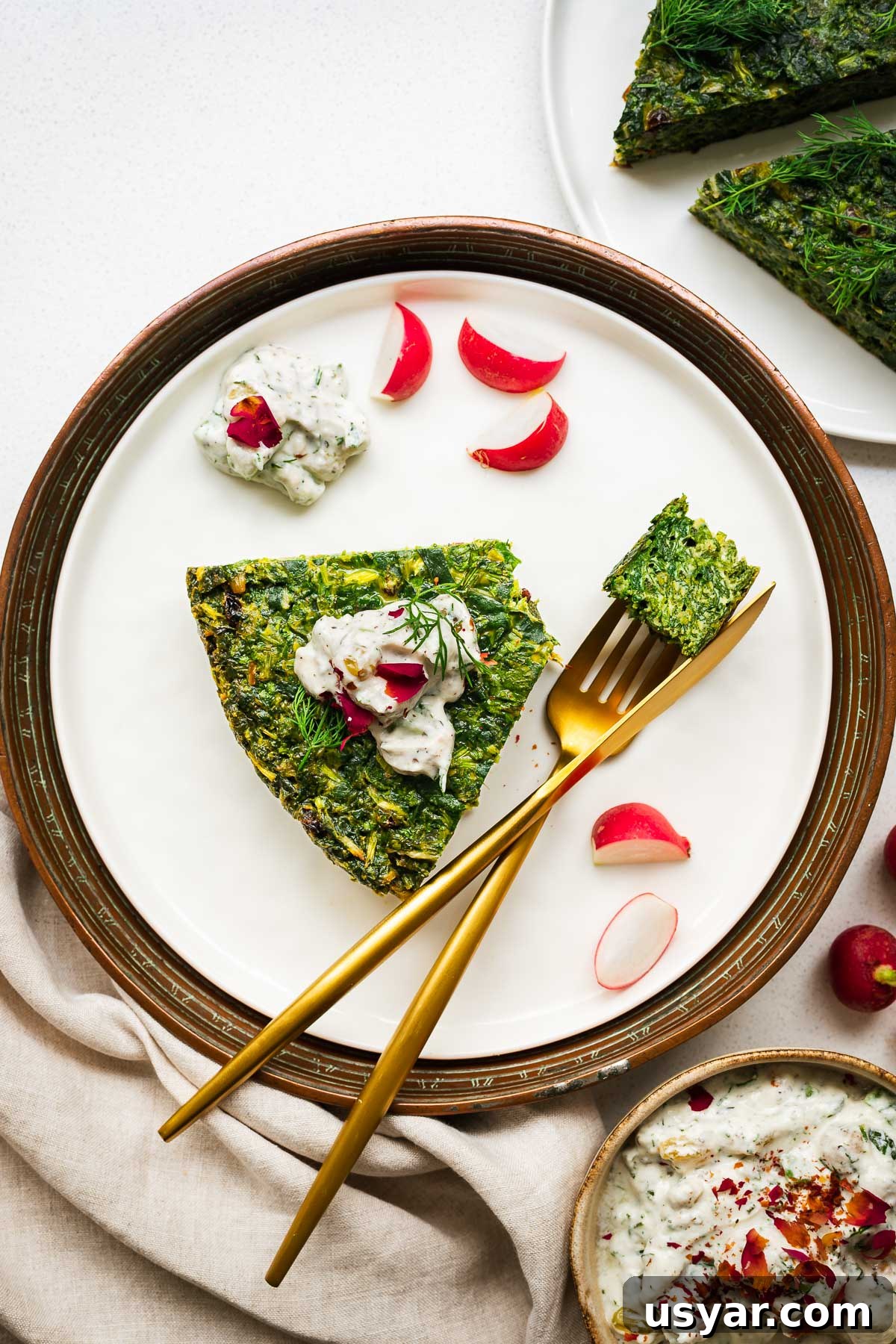 Kuku Sabzi Persian Herb Frittata Recipe 13 A slice of kuku sabzi (Persian herb frittata) with mast-o khiar (Persian cucumber yoghurt) on a plate with golden cutlery.