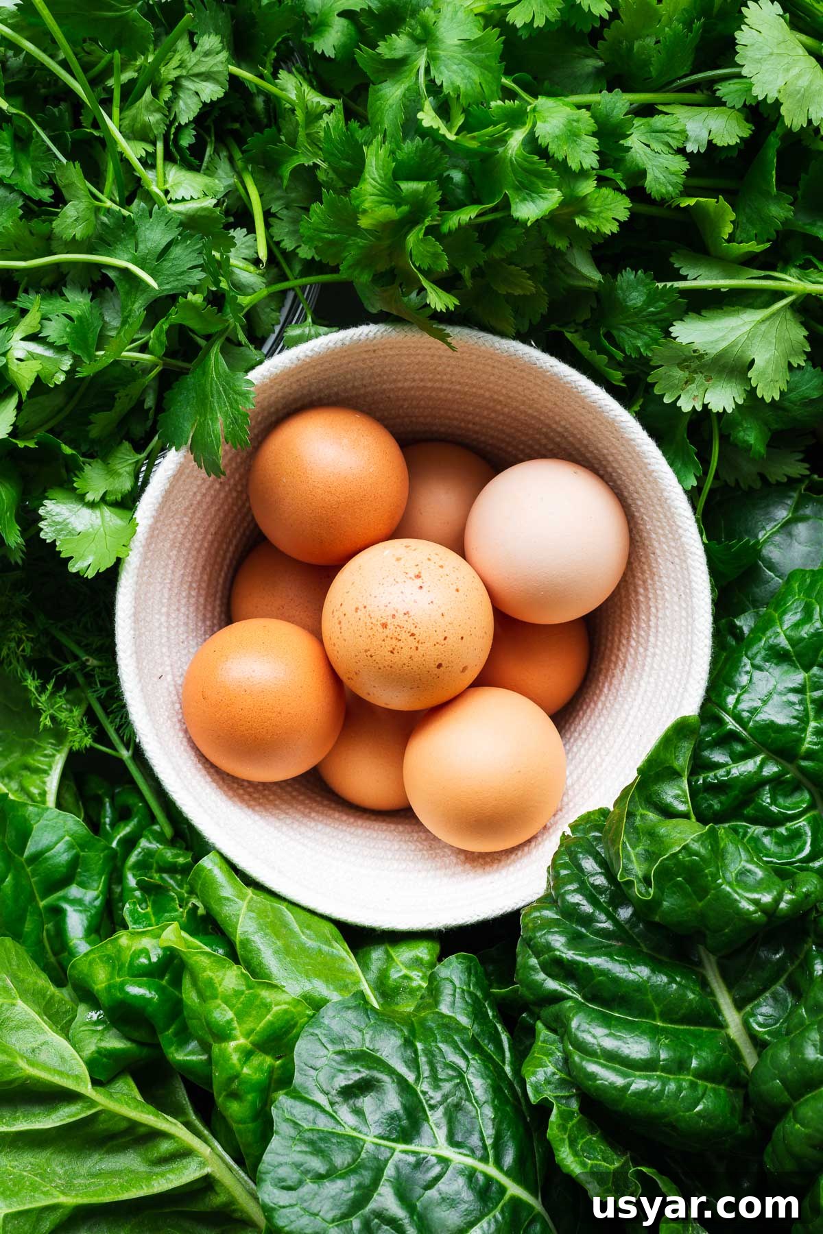 Kuku Sabzi Persian Herb Frittata Recipe 3 The main ingredients for kuku sabzi. A basket of eggs surrounded by fresh herbs and greens, viewed top down.