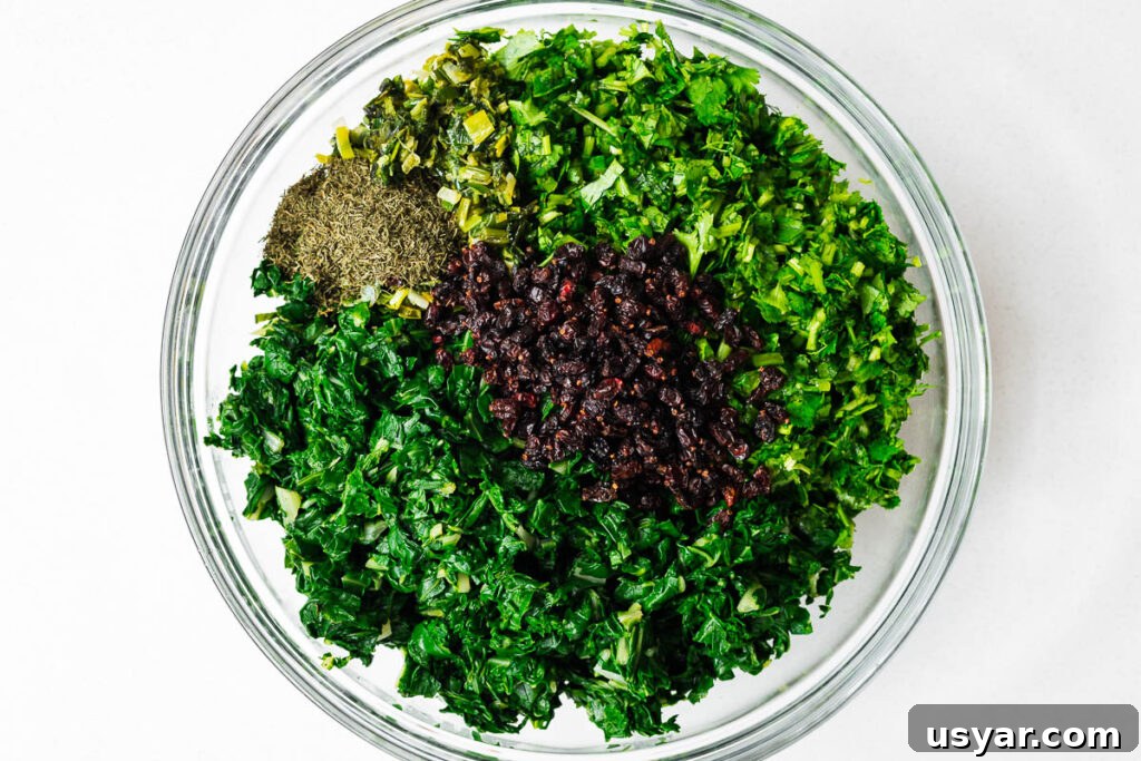 Kuku Sabzi Persian Herb Frittata Recipe 8 The finely chopped herbs, blanched chard, dried dill, cooked leek and barberries for making kuku sabzi viewed from above in a glass bowl.