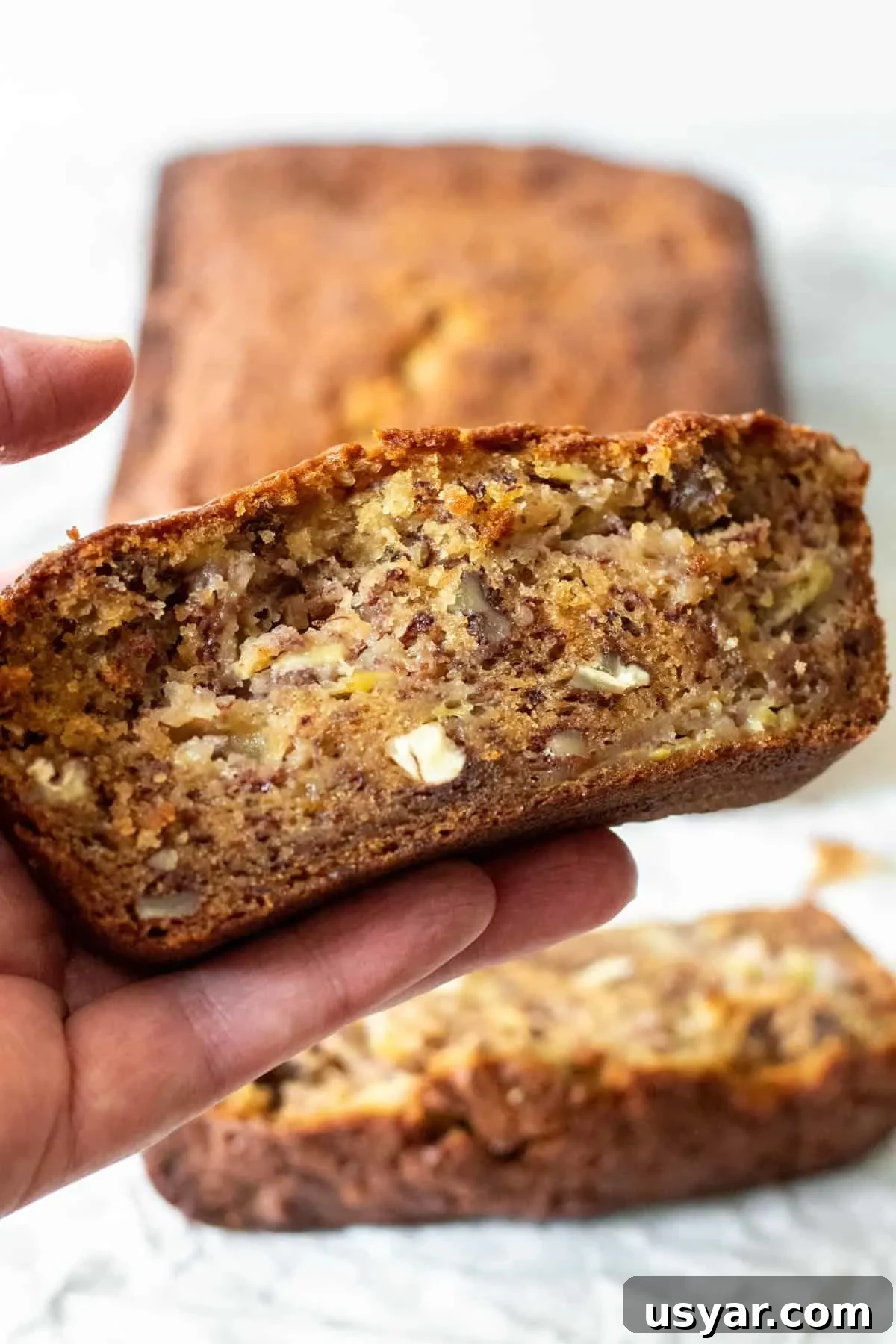 Moist Banana Bread Recipe with Ripe Bananas 6 Hand holding a slice of banana bread with loaf in background.