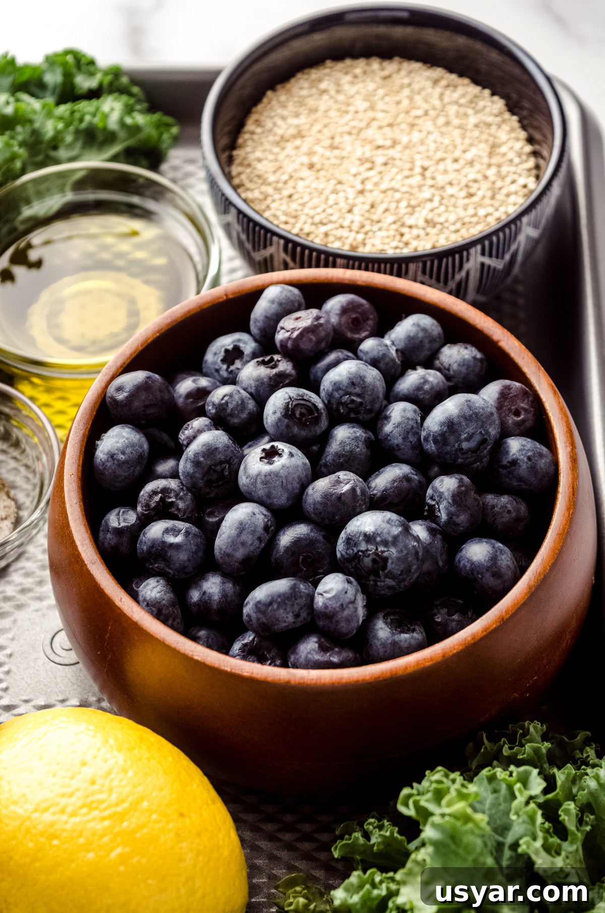 A bowl of blueberries on a surface with a lemon, quinoa, and olive oil in bowls around it.