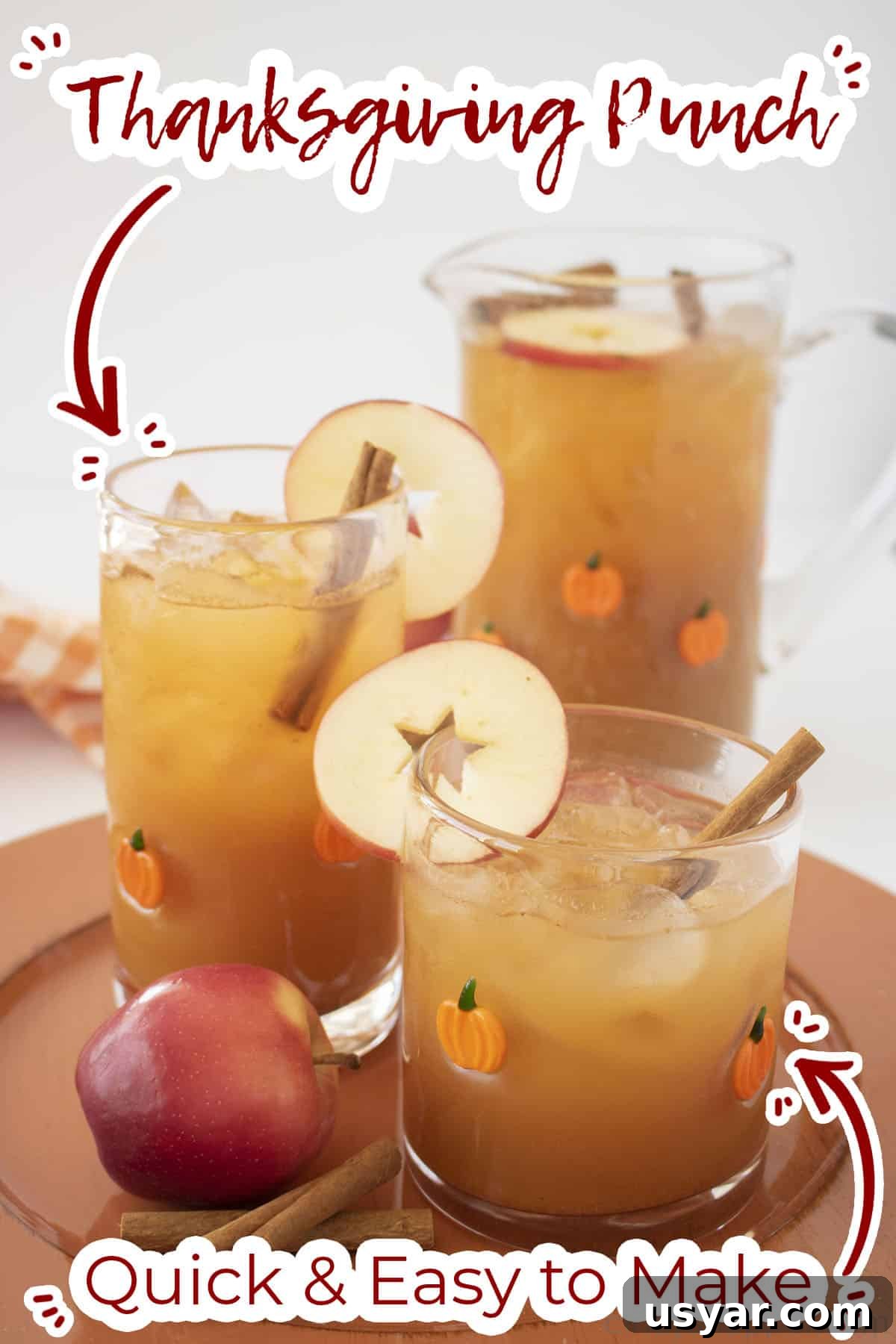 Thanksgiving Punch in two glasses and a pitcher with apples and cinnamon sticks.