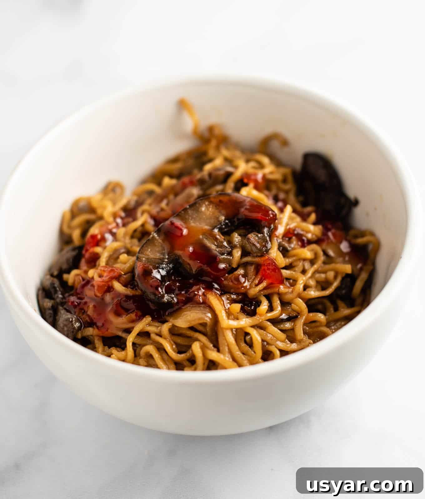 Umami Mushroom Ramen Noodles with Savory Broth 9 mushroom noodles with sweet chili sauce on top in a white bowl