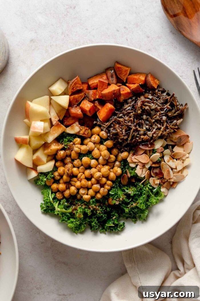 Overhead view of a harvest bowl with kale, chickpeas, apple, almonds and wild rice.