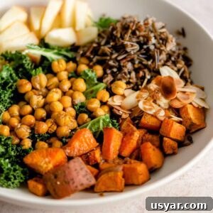 A bowl with roasted sweet potato cubes, chickpeas, apple, wild rice, slivered almonds and kale.