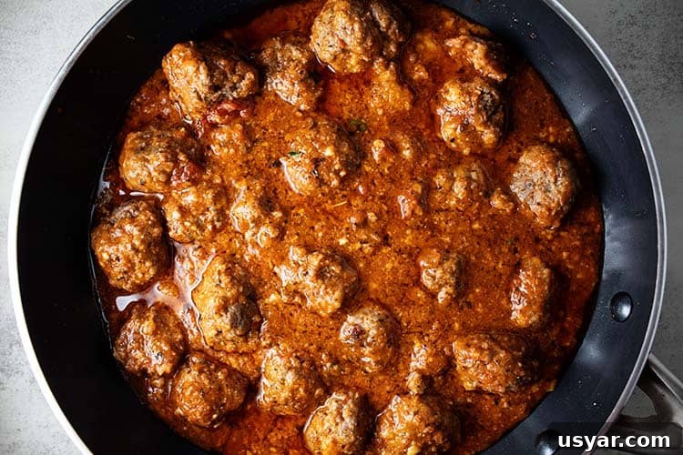 overhead view of cooked keto meatballs with marinara sauce added cooking on stovetop in a black skillet
