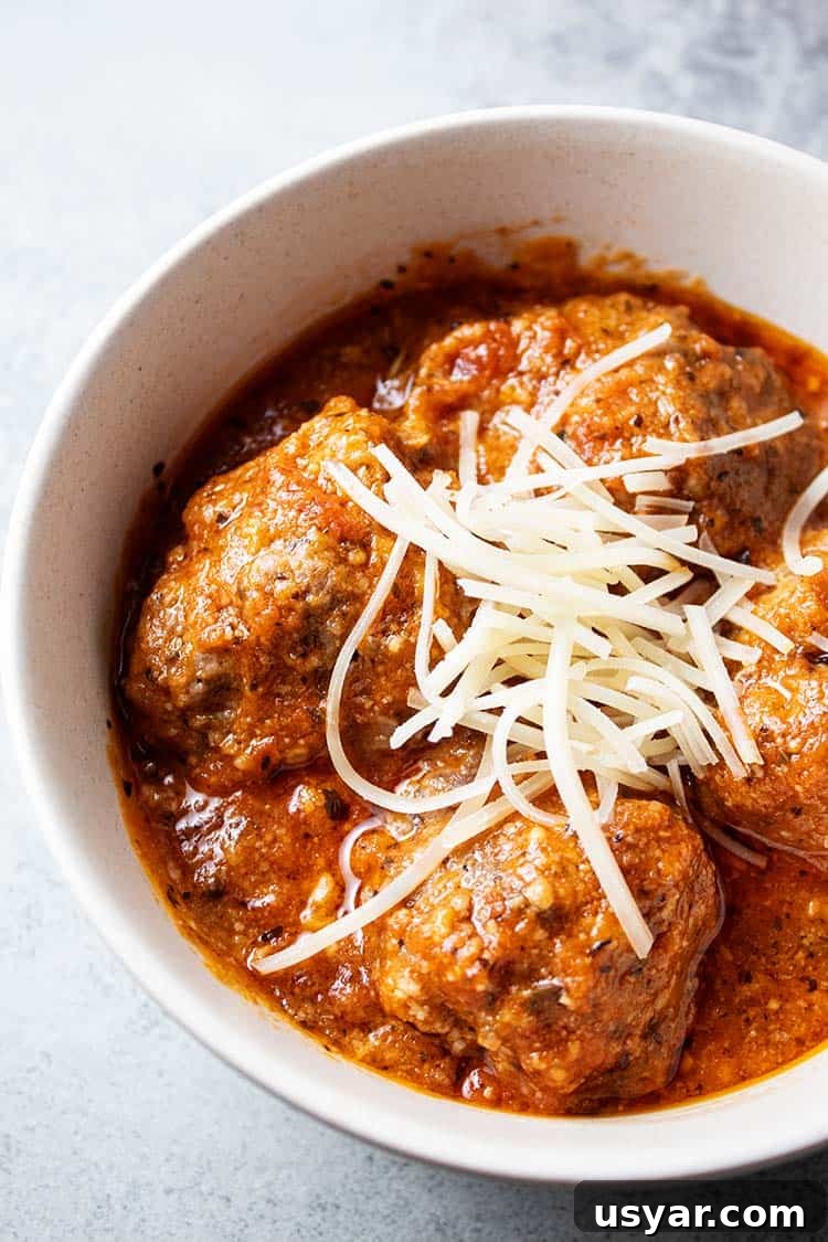 overhead view of keto meatlballs in marinara sauce topped with shredded parmesan cheese in a white serving bowl