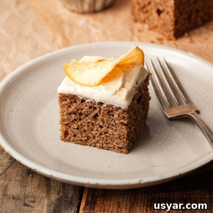 a slice of gluten free applesauce cake topped with cream cheese frosting and an apple chip on a plate with a fork
