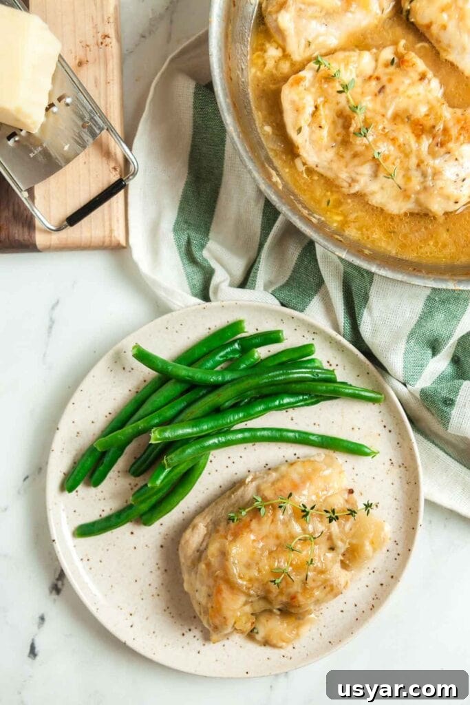 French Onion Skillet Chicken Breasts 2 Overhead view of a plate of skillet French onion chicken breasts smothered with gruyere cheese and served with steamed green beans.