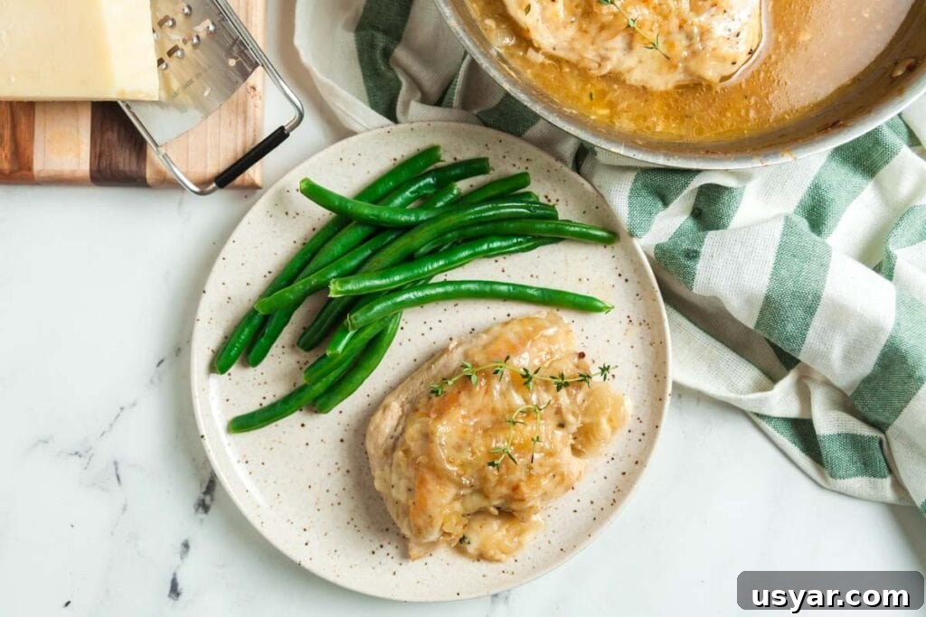 French Onion Skillet Chicken Breasts 7 Serving up a plate of skillet French onion chicken, a block of gruyere and a cheese grater are on a cutting board to the side.