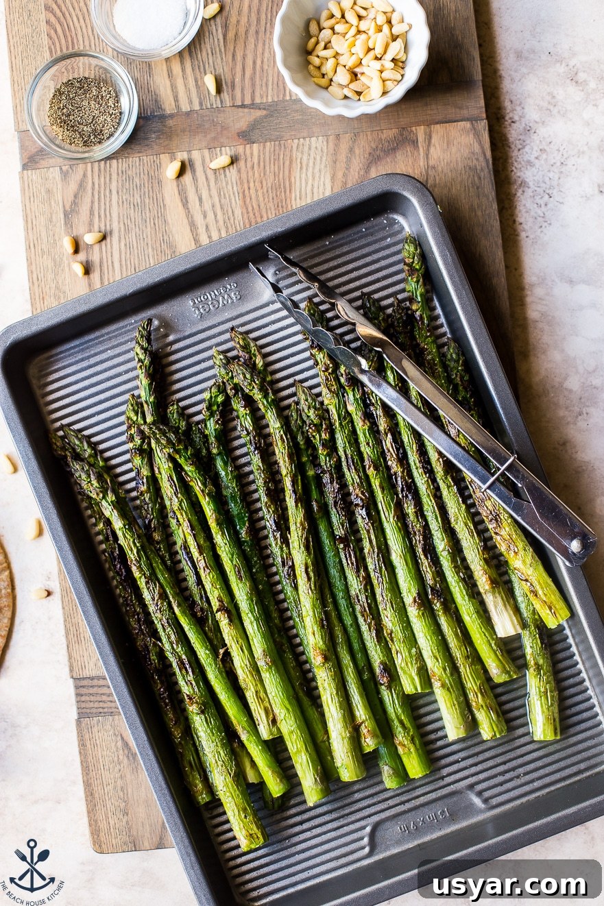 Charred Grilled Asparagus Salad with Lemon Vinaigrette 4 Overhead photo of grilled asparagus on a silver baking sheet with a pair of tongs