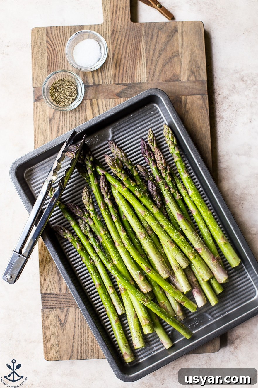 Charred Grilled Asparagus Salad with Lemon Vinaigrette 6 Pre-grilled asparagus on a silver baking sheet with a set of tongs