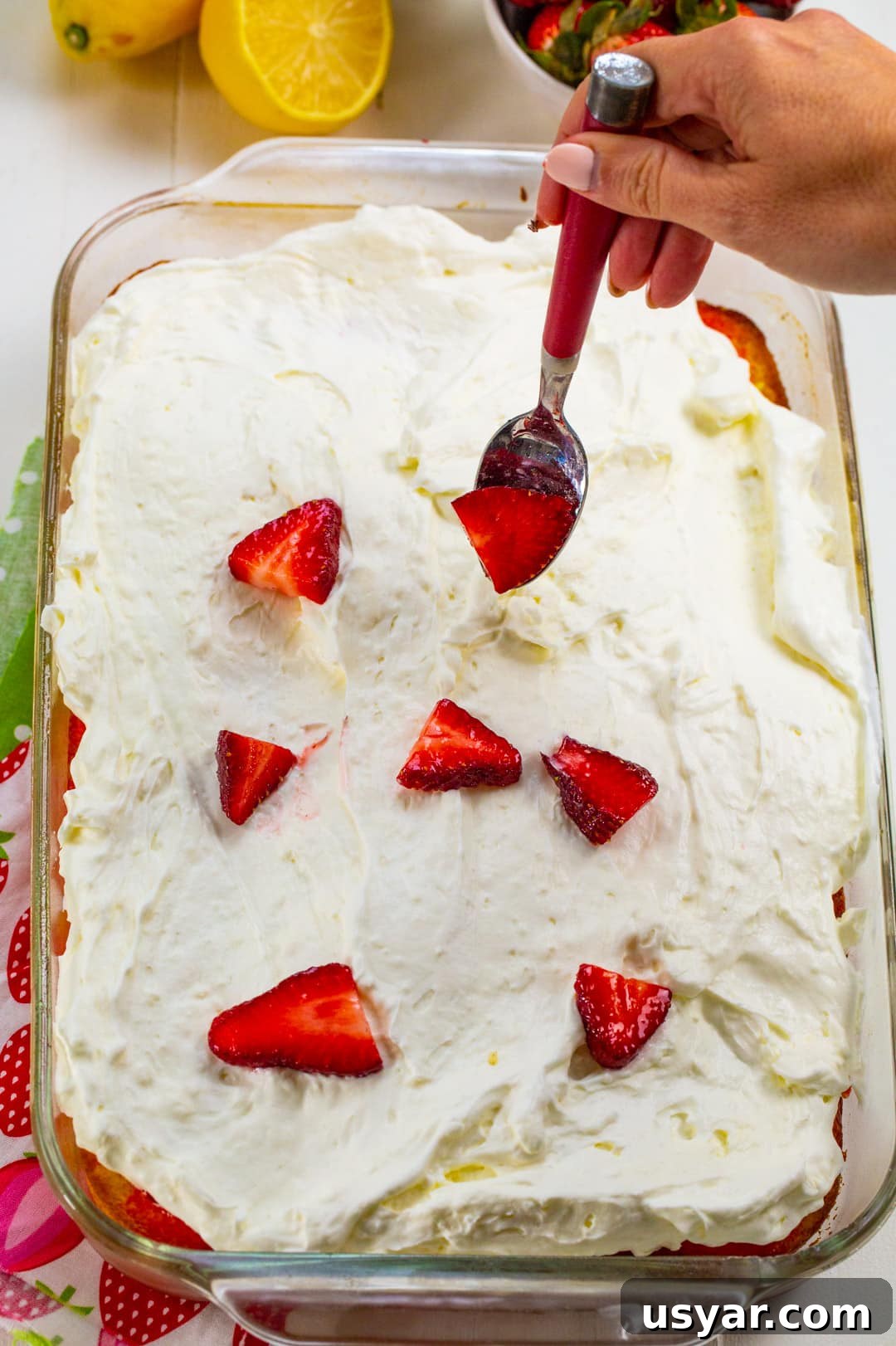 Refreshing Strawberry Lemonade Poke Cake 5 Spooning strawberries on top.