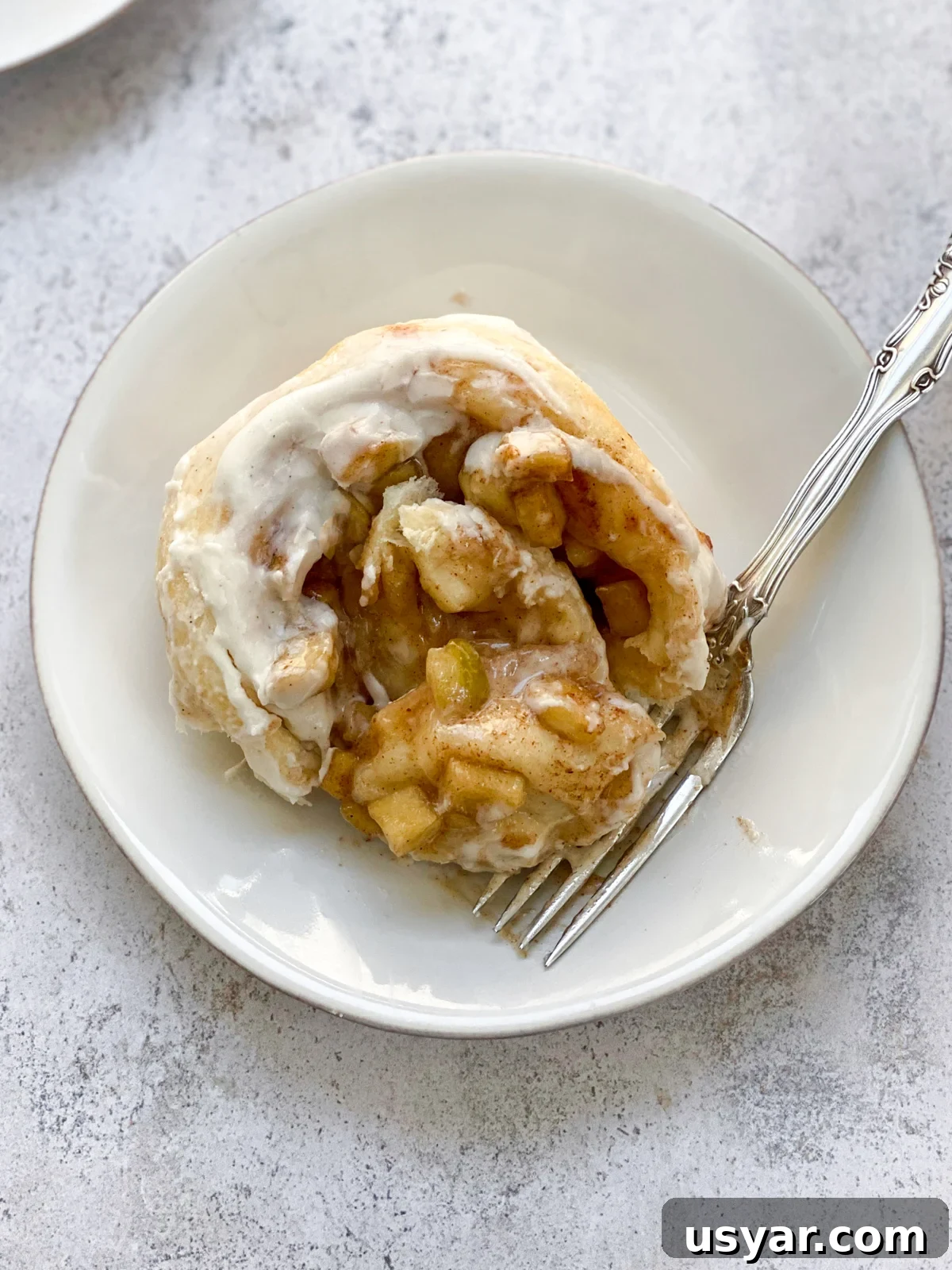 Cinnamon Rolls Stuffed with Apple Pie Filling 2 a cinnamon roll with apple pie filling on a plate with a bite on a fork.