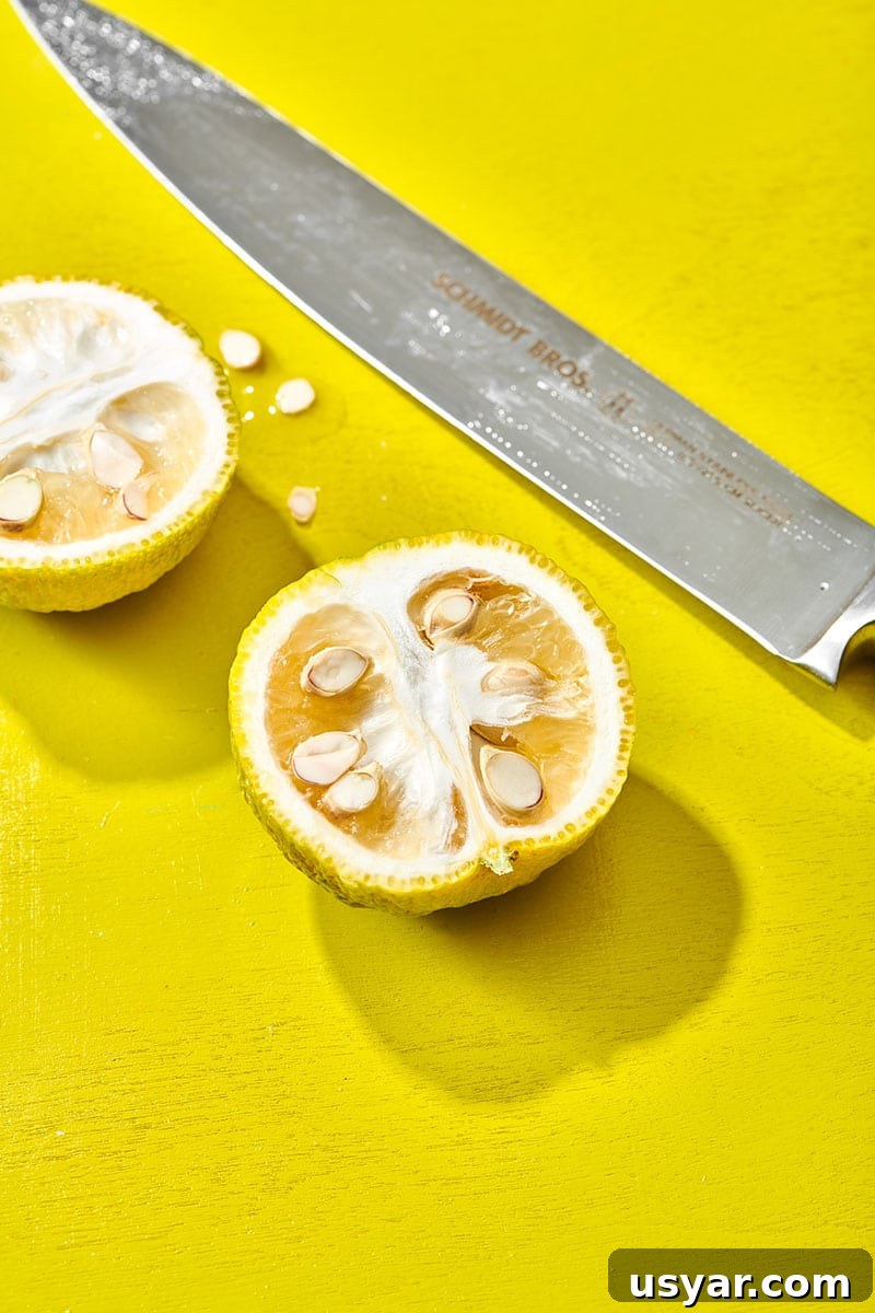 Cut yuzu fruit with chef knife on yellow table.
