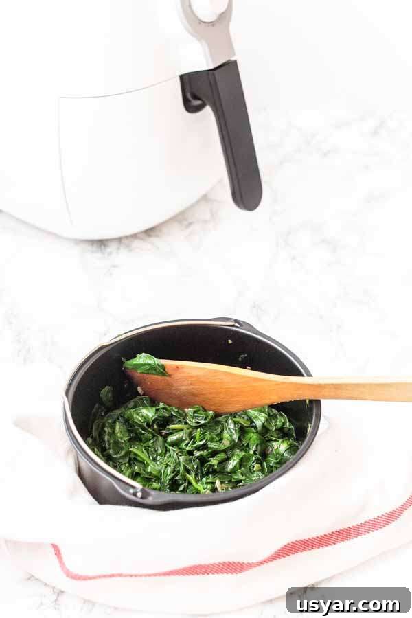 Crispy Garlic Air Fryer Spinach 7 Fresh spinach in an Air Fryer barrel with a wooden spoon for serving the spinach.