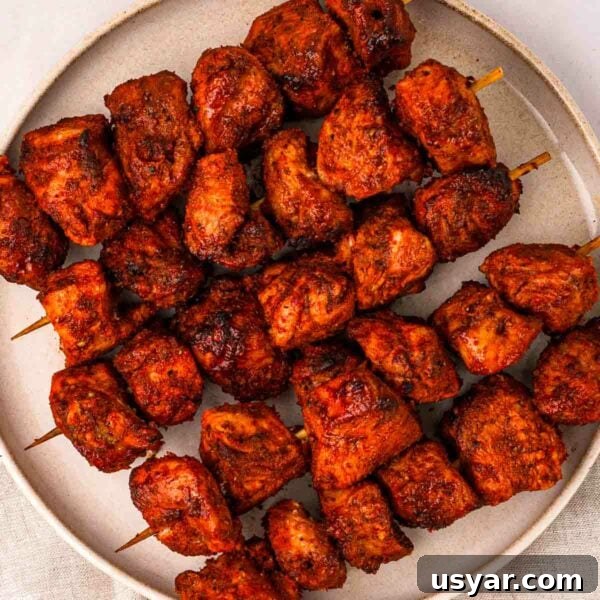 Five skewers with chunks of tandoor chicken on, laying on a plate.