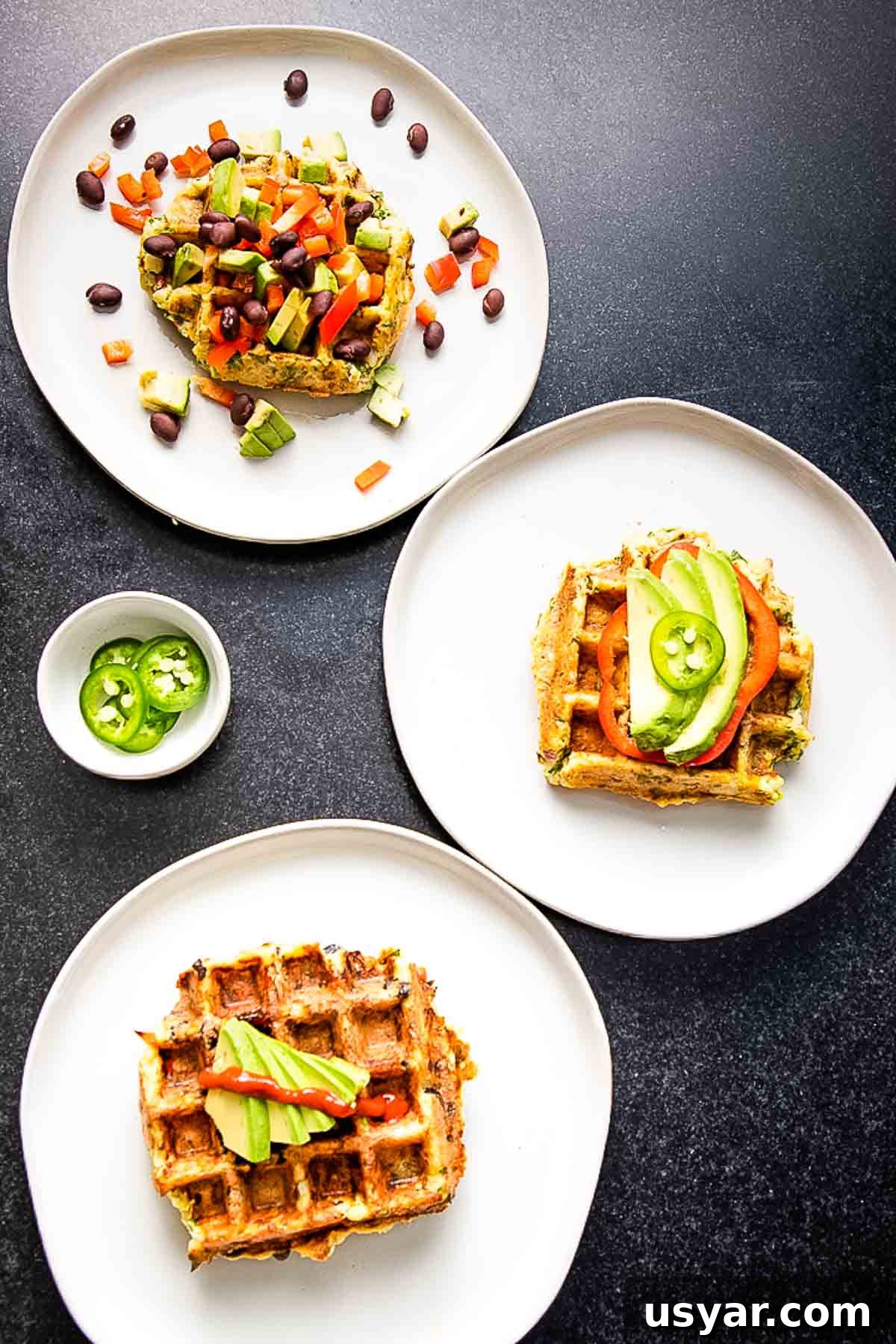 Crispy Leftover Mashed Potato Waffles 2 3 plates of savory waffles with assorted toppings including avocado slices, sriracha, jalapenos, black beans, chopped bell peppers.