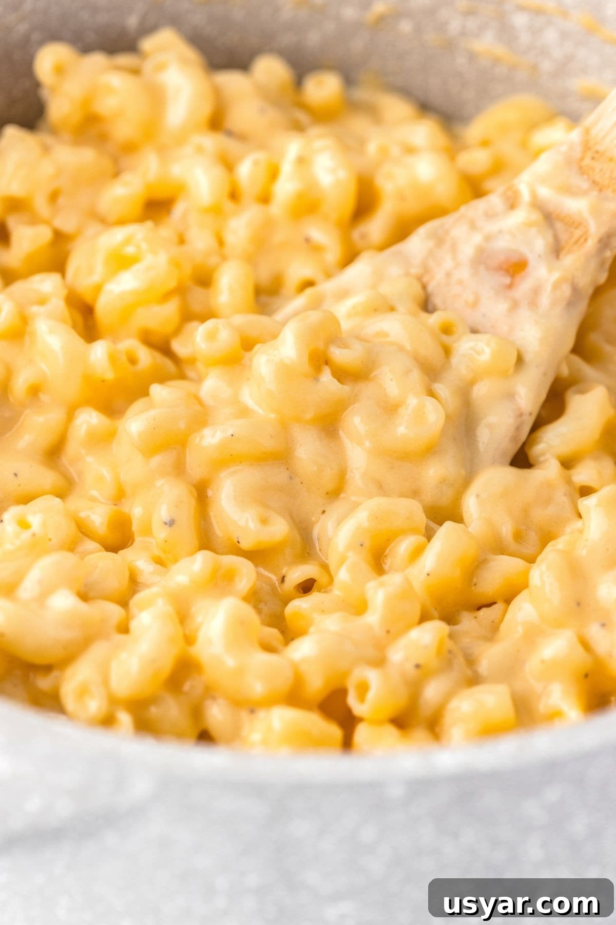 Creamy Stovetop Macaroni and Cheese 2 Creamy macaroni and cheese in a white bowl with a wooden spoon.