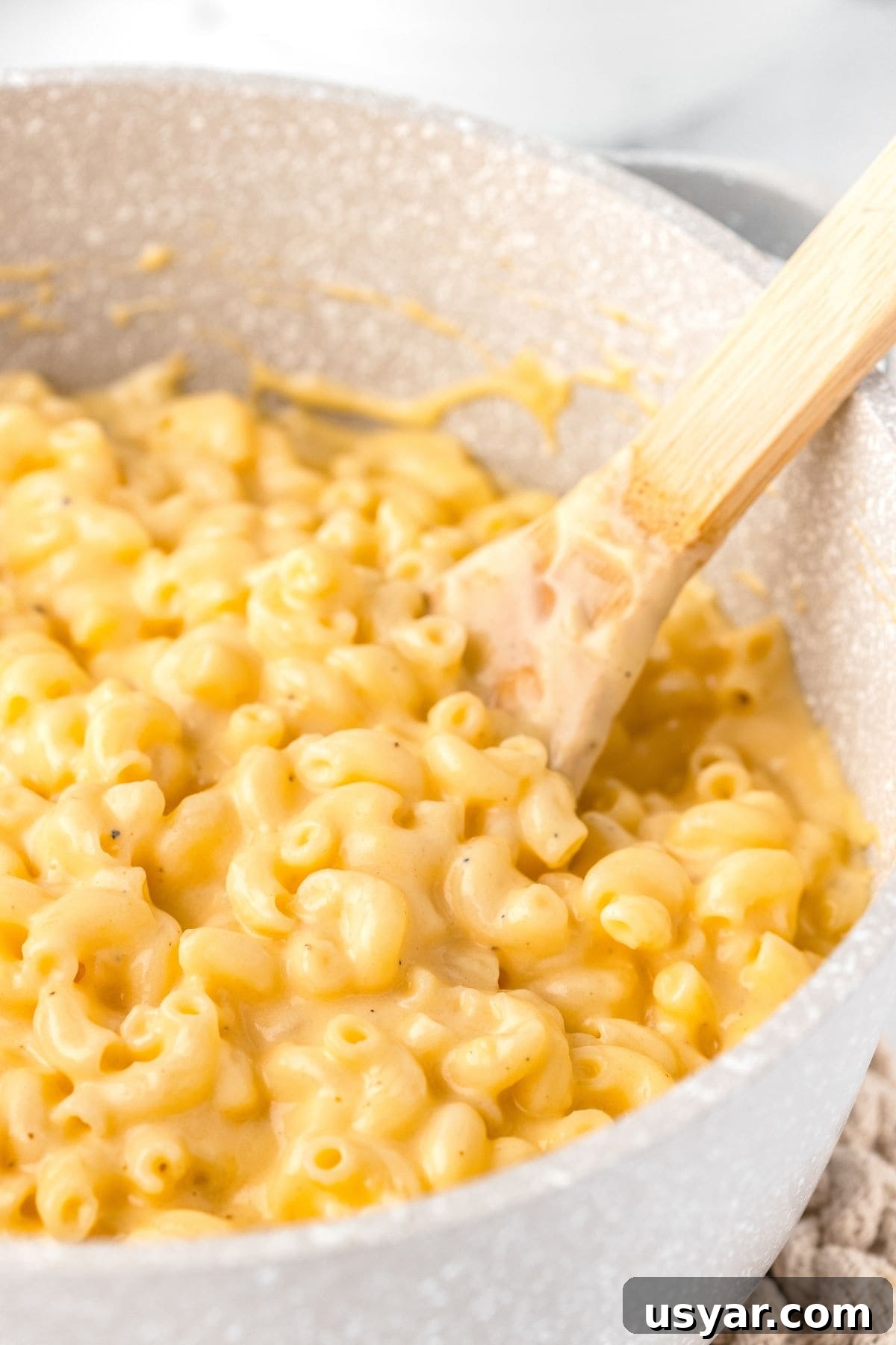 Creamy Stovetop Macaroni and Cheese 3 Creamy macaroni and cheese in a white speckled pot with a wooden spoon.